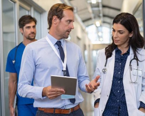 Man and woman doctor having a discussion in hospital hallway while holding digital tablet. Doctor discussing patient case status with his medical staff after operation. Pharmaceutical representative showing medical report.